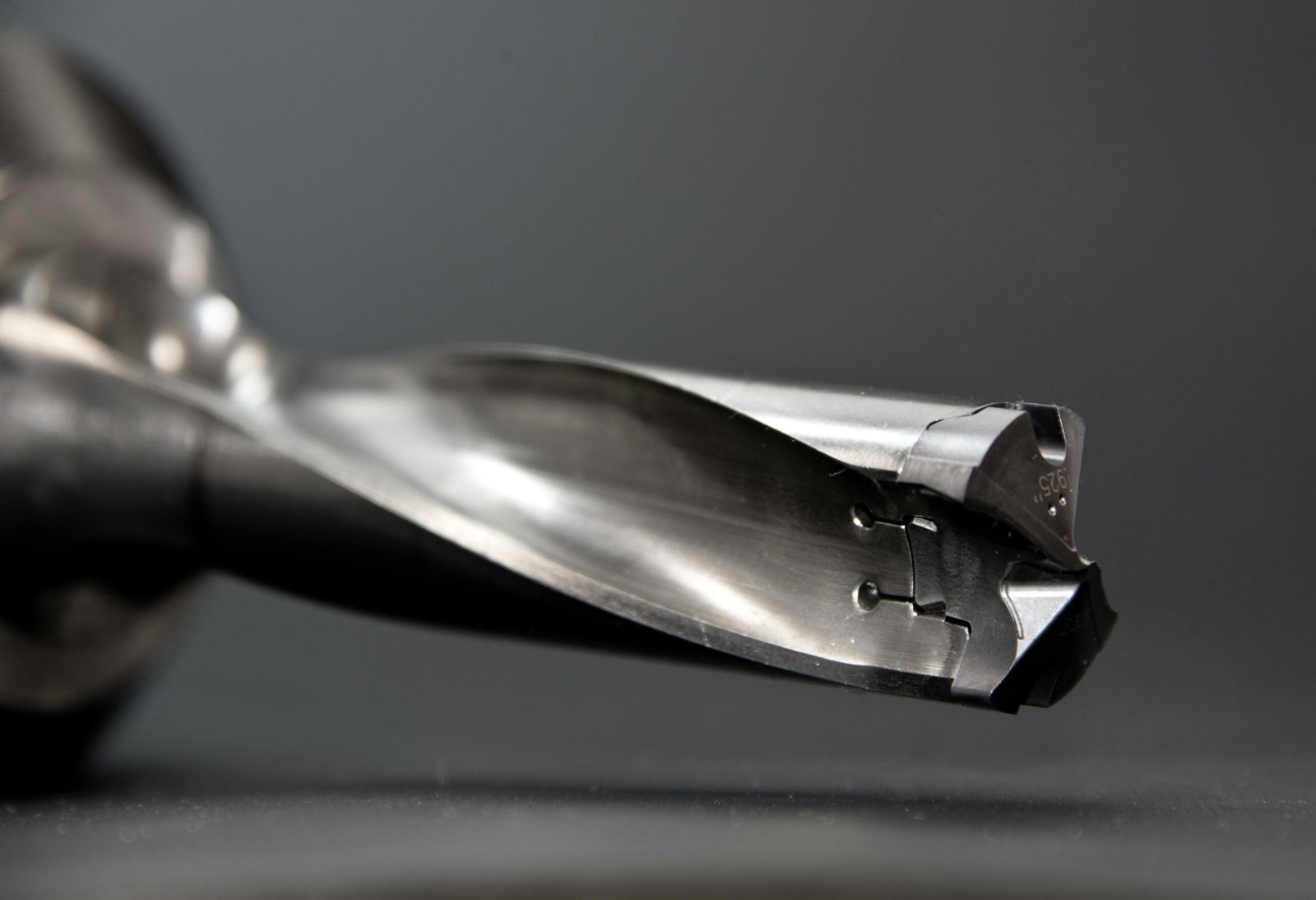 Macro shot of a sharp, clean drill bit with a spiral flute design against a dark background.

